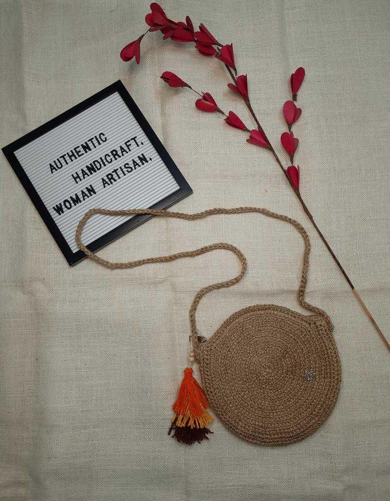 A round crocheted jute bag with a terracotta tassel, laid on hessian