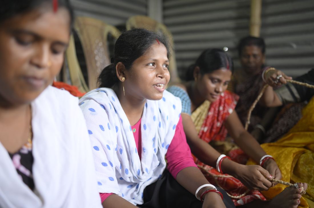 Women of the collective seated close together, braiding jute rope and talking