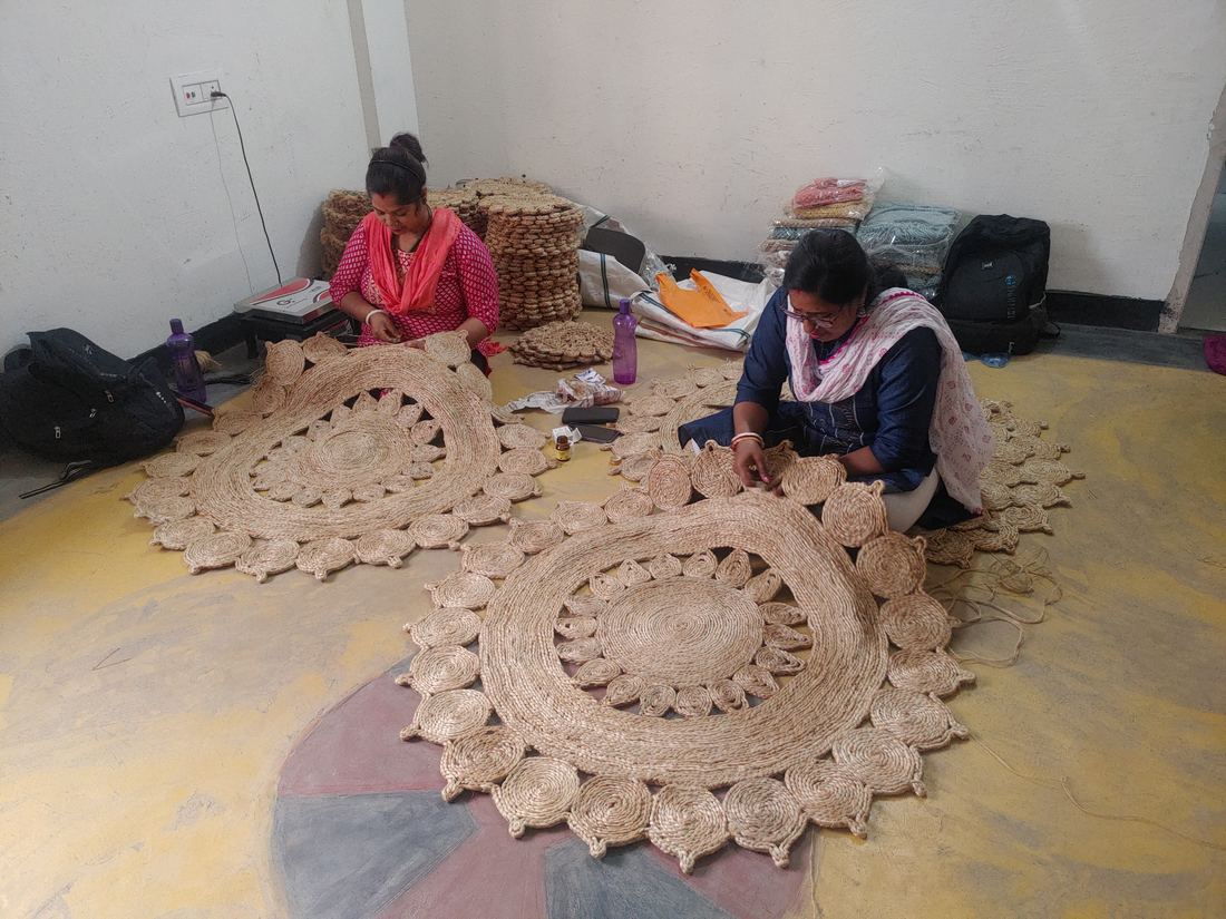 Two artisans stitching braided jute into circular mats