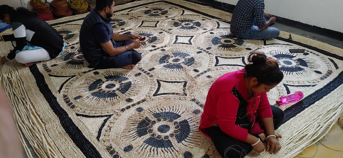 Artisans kneeling around a room-sized jute floor piece patterned with medallions